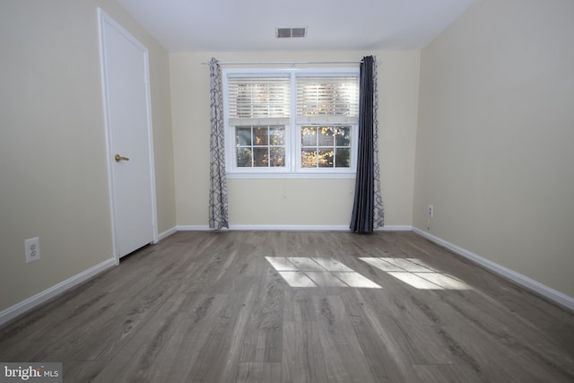 empty room with wood finished floors, visible vents, and baseboards