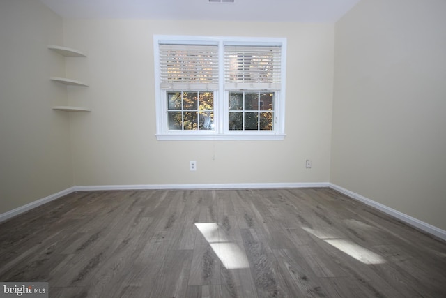 empty room featuring visible vents, wood finished floors, and baseboards