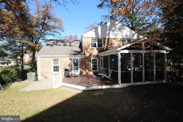 back of property with central air condition unit, a lawn, brick siding, and a sunroom