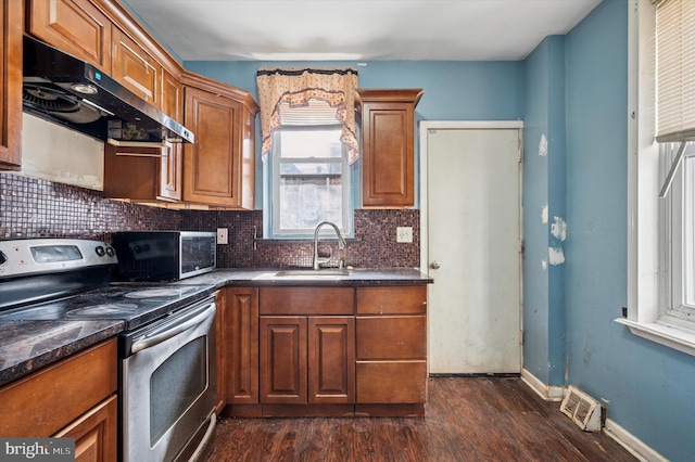 kitchen with dark countertops, stainless steel electric range, under cabinet range hood, and a sink