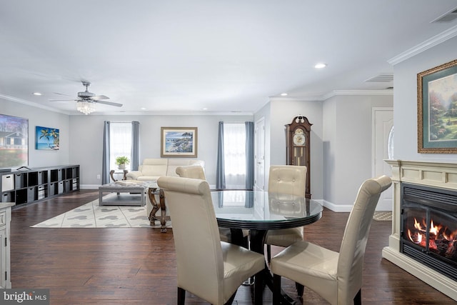 dining area featuring visible vents, dark wood-type flooring, a glass covered fireplace, crown molding, and baseboards