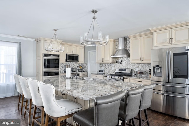 kitchen with appliances with stainless steel finishes, cream cabinets, wall chimney range hood, and a sink