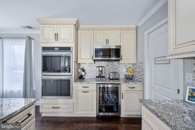 kitchen featuring light stone counters, beverage cooler, ornamental molding, appliances with stainless steel finishes, and cream cabinets