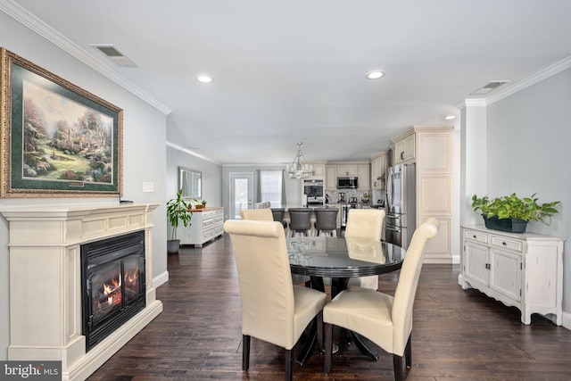 dining space featuring dark wood-style floors, visible vents, crown molding, and a glass covered fireplace