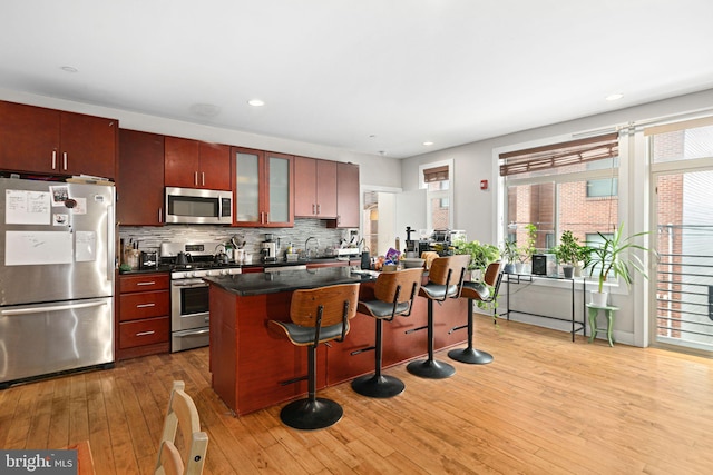 kitchen featuring light wood finished floors, glass insert cabinets, a breakfast bar, decorative backsplash, and stainless steel appliances