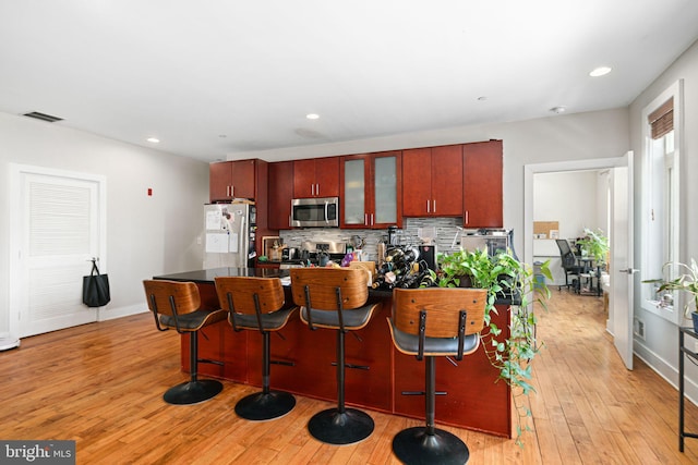 kitchen with visible vents, a breakfast bar, stainless steel appliances, tasteful backsplash, and light wood-type flooring