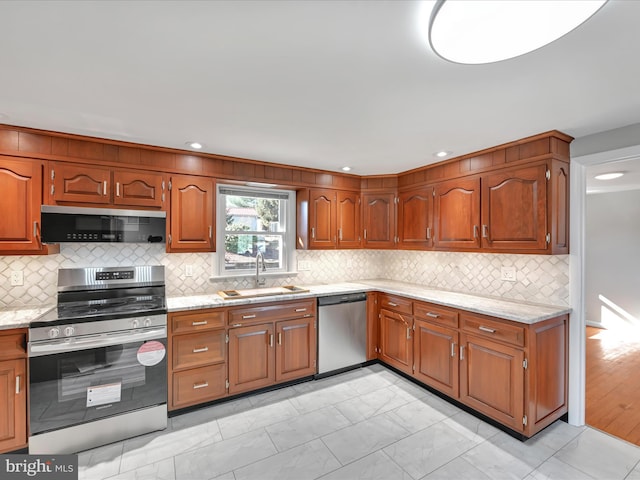 kitchen featuring marble finish floor, a sink, stainless steel appliances, brown cabinetry, and light stone countertops