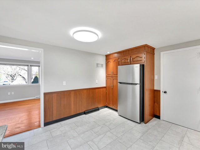 kitchen with wooden walls, marble finish floor, wainscoting, and freestanding refrigerator