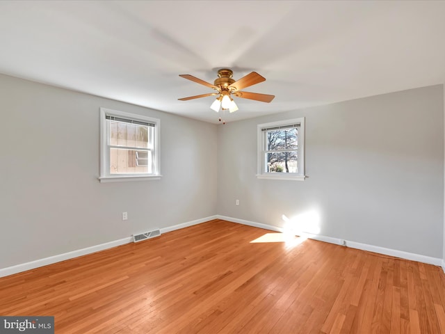 spare room with light wood finished floors, visible vents, a ceiling fan, and baseboards