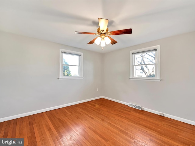 empty room featuring hardwood / wood-style floors, baseboards, visible vents, and a ceiling fan