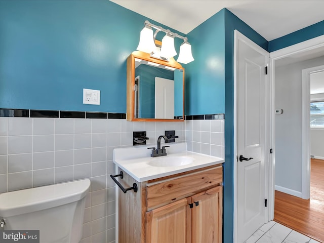 half bath with marble finish floor, toilet, tile walls, and vanity