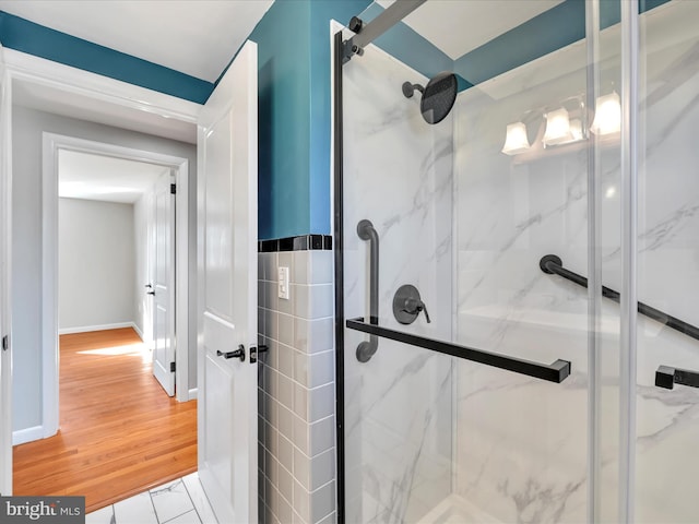 bathroom featuring a marble finish shower, baseboards, and wood finished floors