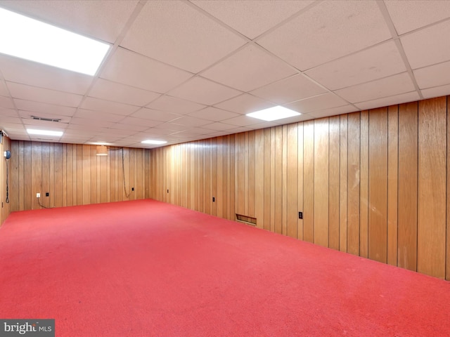 finished below grade area featuring visible vents, carpet, wooden walls, and a drop ceiling