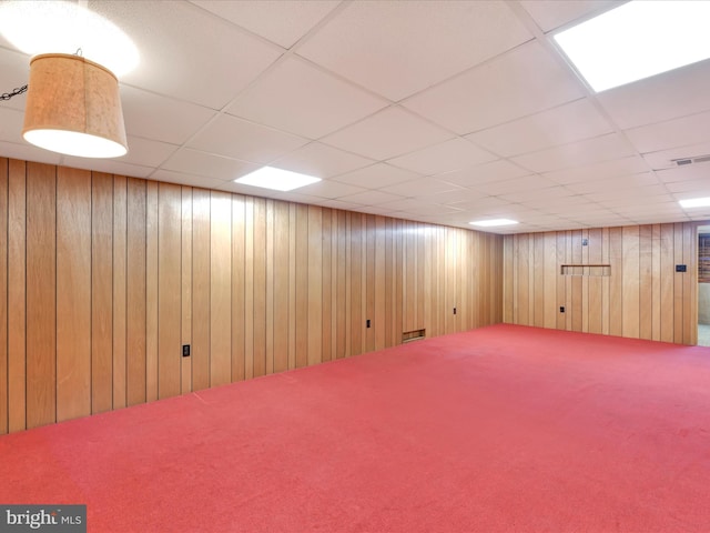 finished basement with carpet, a paneled ceiling, visible vents, and wood walls