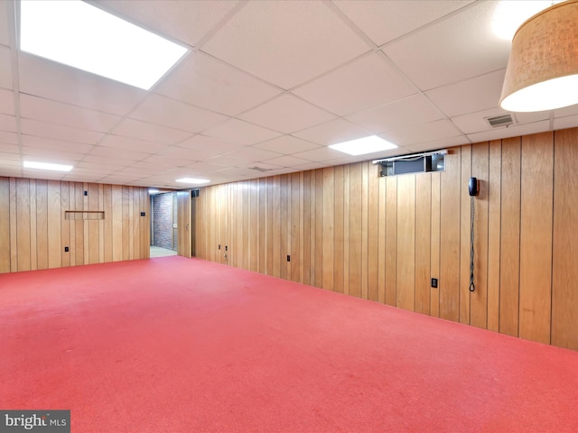 finished basement featuring visible vents, wood walls, carpet, and a drop ceiling