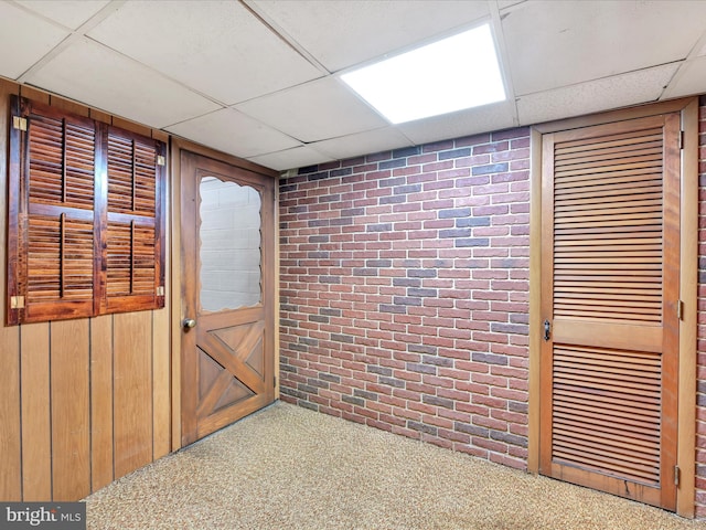 interior space with a drop ceiling, carpet, and brick wall