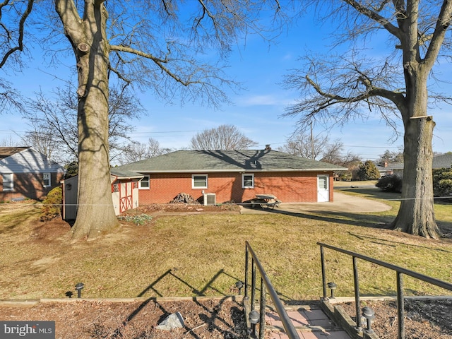 back of house featuring central air condition unit, fence, a lawn, and brick siding