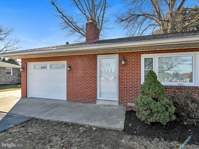 view of front of house with driveway, brick siding, an attached garage, and a chimney