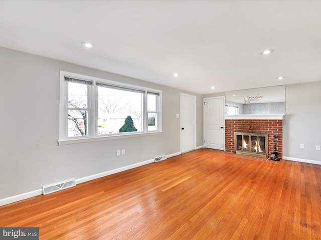 unfurnished living room with visible vents, baseboards, recessed lighting, light wood-style floors, and a brick fireplace