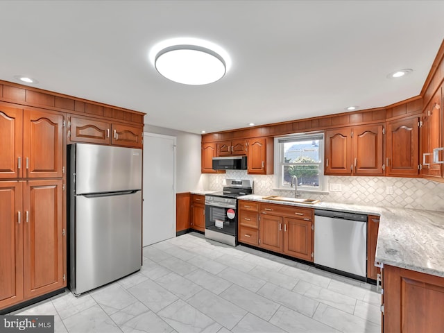 kitchen with tasteful backsplash, light stone counters, appliances with stainless steel finishes, brown cabinetry, and a sink