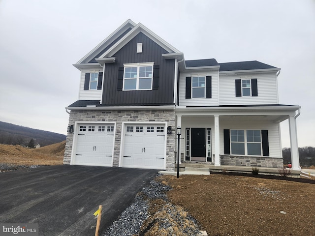 craftsman inspired home featuring board and batten siding, covered porch, stone siding, and driveway