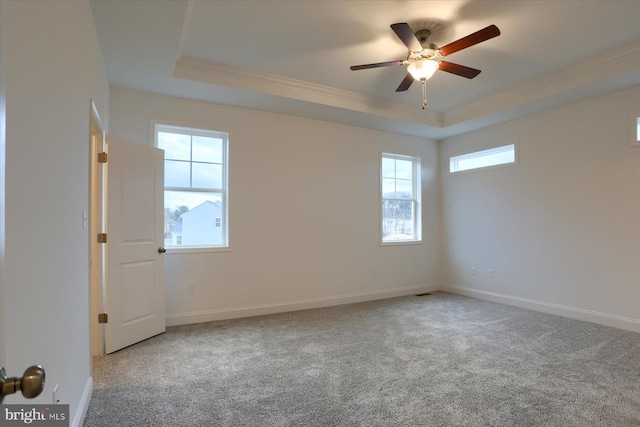 carpeted spare room featuring a tray ceiling, baseboards, ceiling fan, and crown molding