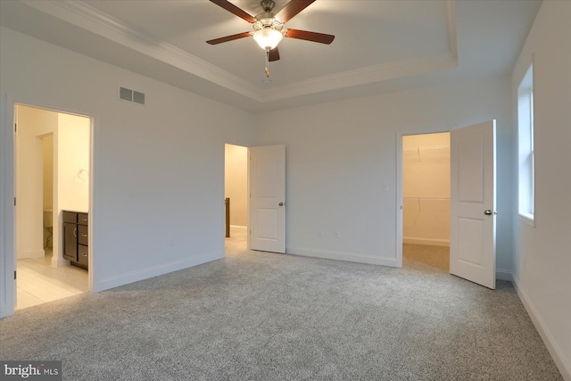 unfurnished bedroom with a walk in closet, a raised ceiling, visible vents, and light carpet