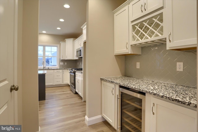 kitchen with a sink, white cabinetry, wine cooler, appliances with stainless steel finishes, and light stone countertops