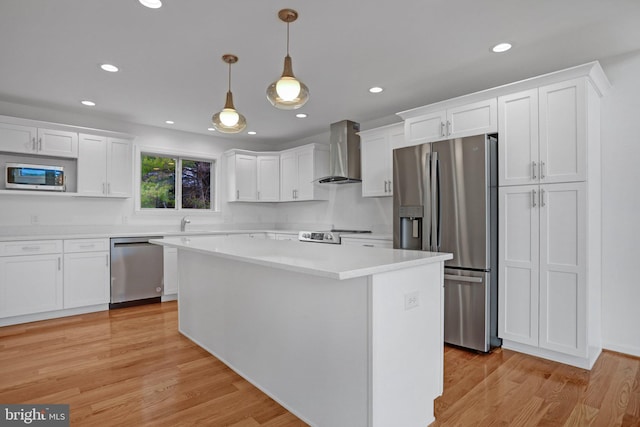 kitchen featuring light wood finished floors, appliances with stainless steel finishes, wall chimney exhaust hood, and white cabinetry