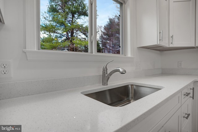 kitchen featuring white cabinetry, light stone counters, a wealth of natural light, and a sink