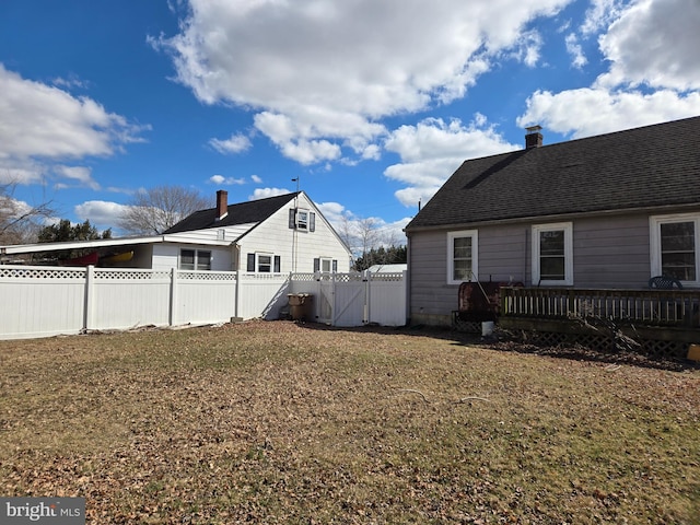 exterior space featuring a gate, a wooden deck, a fenced backyard, a chimney, and a lawn