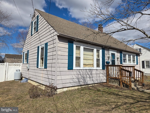 view of side of home featuring a yard, roof with shingles, a chimney, and fence