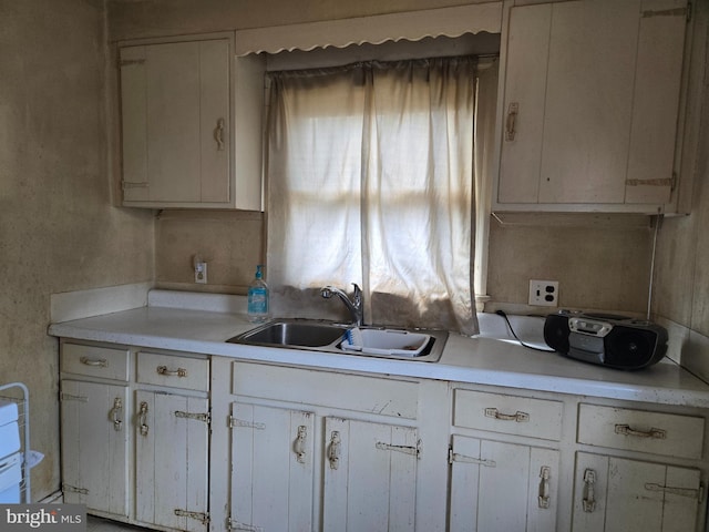 kitchen with white cabinetry, light countertops, and a sink