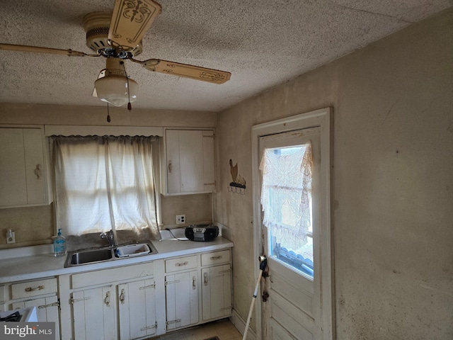 kitchen with light countertops, white cabinets, a ceiling fan, and a sink