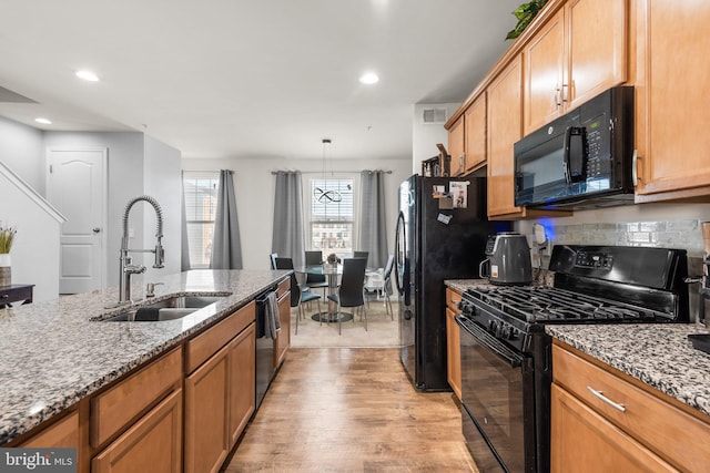 kitchen featuring visible vents, black appliances, a sink, light stone counters, and light wood finished floors