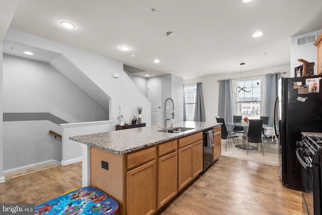 kitchen with light wood-type flooring, an island with sink, light stone counters, black appliances, and a sink