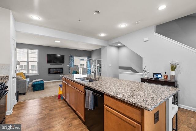 kitchen featuring open floor plan, light stone counters, wood finished floors, black appliances, and a sink