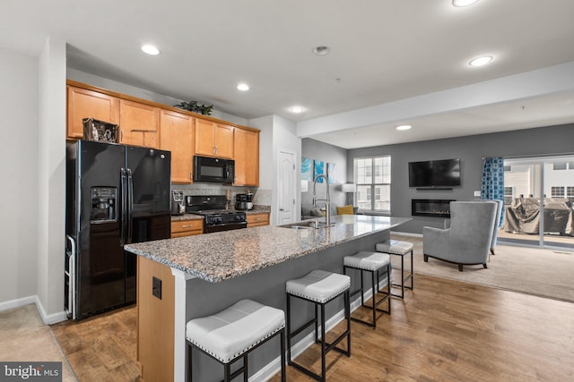 kitchen featuring light wood finished floors, open floor plan, a breakfast bar, black appliances, and a sink