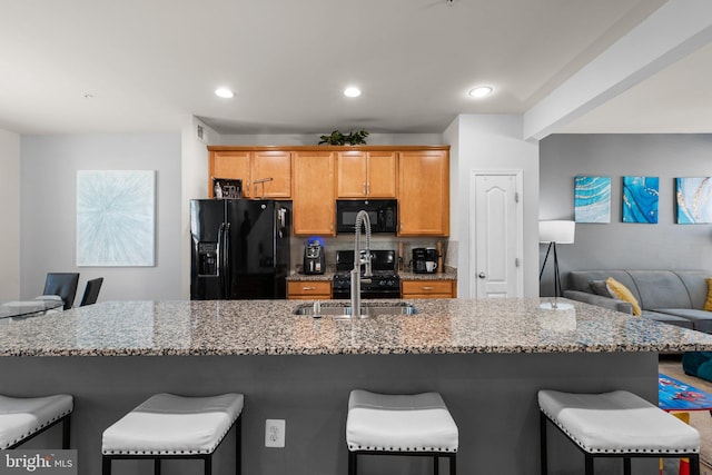 kitchen featuring a sink, a kitchen breakfast bar, black appliances, and light stone countertops