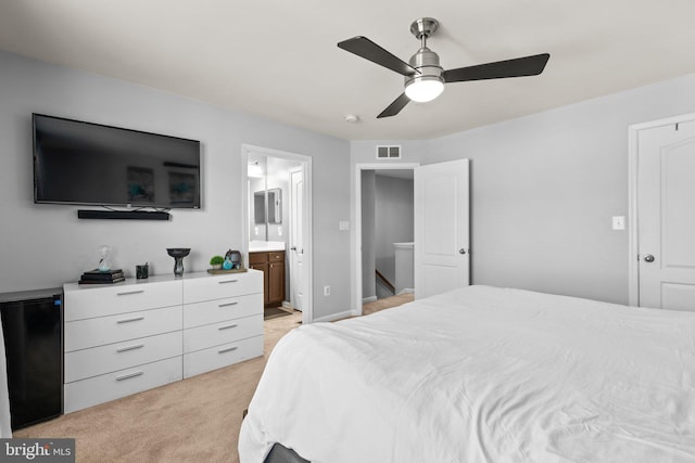 bedroom featuring visible vents, ceiling fan, light colored carpet, refrigerator, and ensuite bath