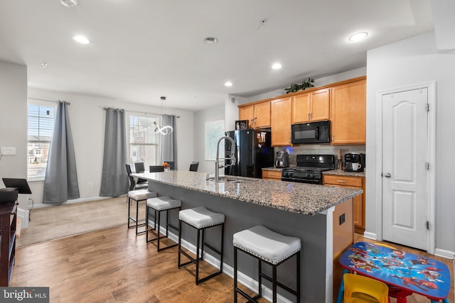 kitchen with light stone countertops, an island with sink, black appliances, a kitchen breakfast bar, and light wood-type flooring