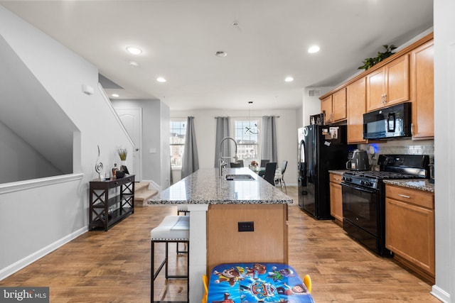 kitchen featuring light wood-style flooring, black appliances, a kitchen bar, and a sink