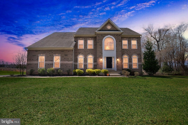 colonial inspired home featuring a shingled roof, a front yard, and brick siding