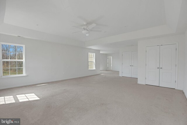 unfurnished bedroom featuring two closets, carpet flooring, baseboards, a raised ceiling, and ceiling fan
