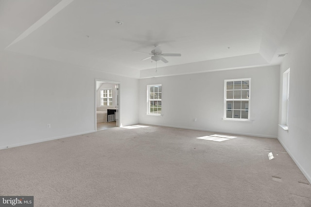 unfurnished living room with a tray ceiling, ceiling fan, and light carpet