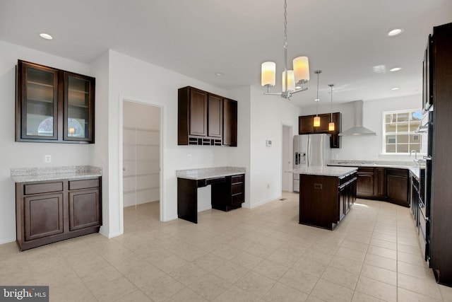 kitchen featuring wall chimney exhaust hood, dark brown cabinetry, stainless steel fridge with ice dispenser, a center island, and a notable chandelier