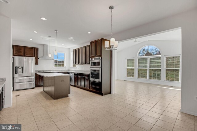 kitchen featuring dark brown cabinetry, a kitchen island, open floor plan, stainless steel appliances, and wall chimney range hood