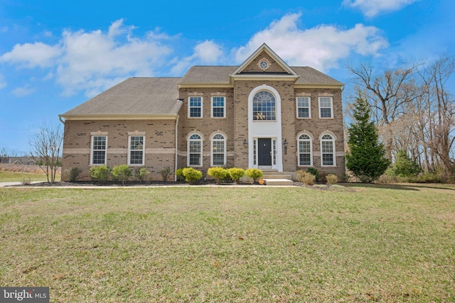 colonial inspired home with a front yard, brick siding, and roof with shingles