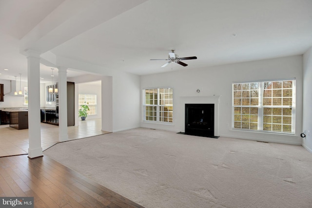 unfurnished living room featuring ornate columns, baseboards, a ceiling fan, and light carpet