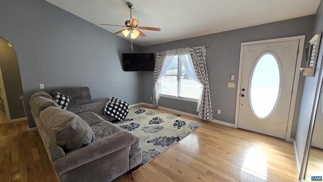 living area with baseboards, vaulted ceiling, light wood-style flooring, arched walkways, and a ceiling fan